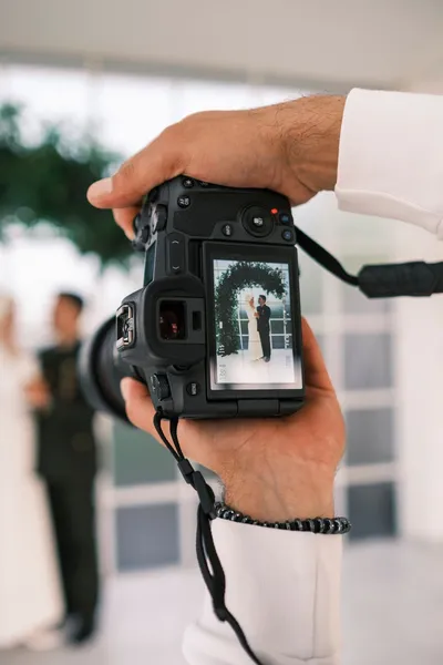 Hands holding a camera whose screen shows a couple in wedding attire.