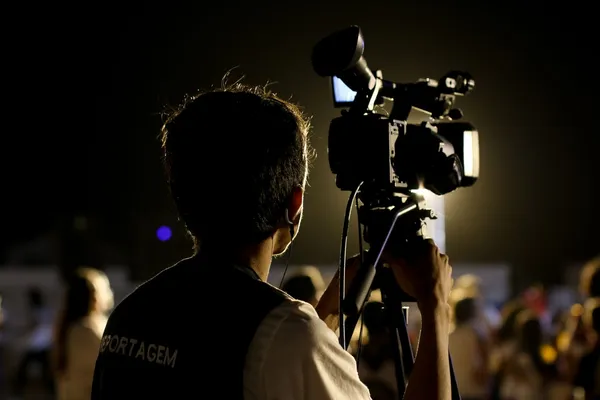 Camera operator seen from behind with a camera on a tripod at an event.