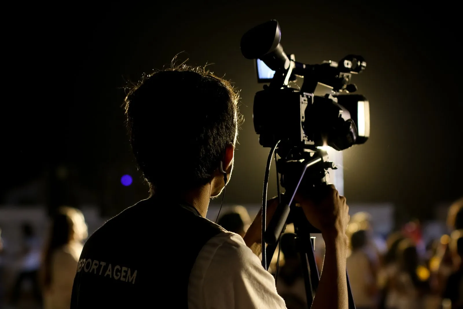 Camera operator seen from behind with a camera on a tripod at an event.