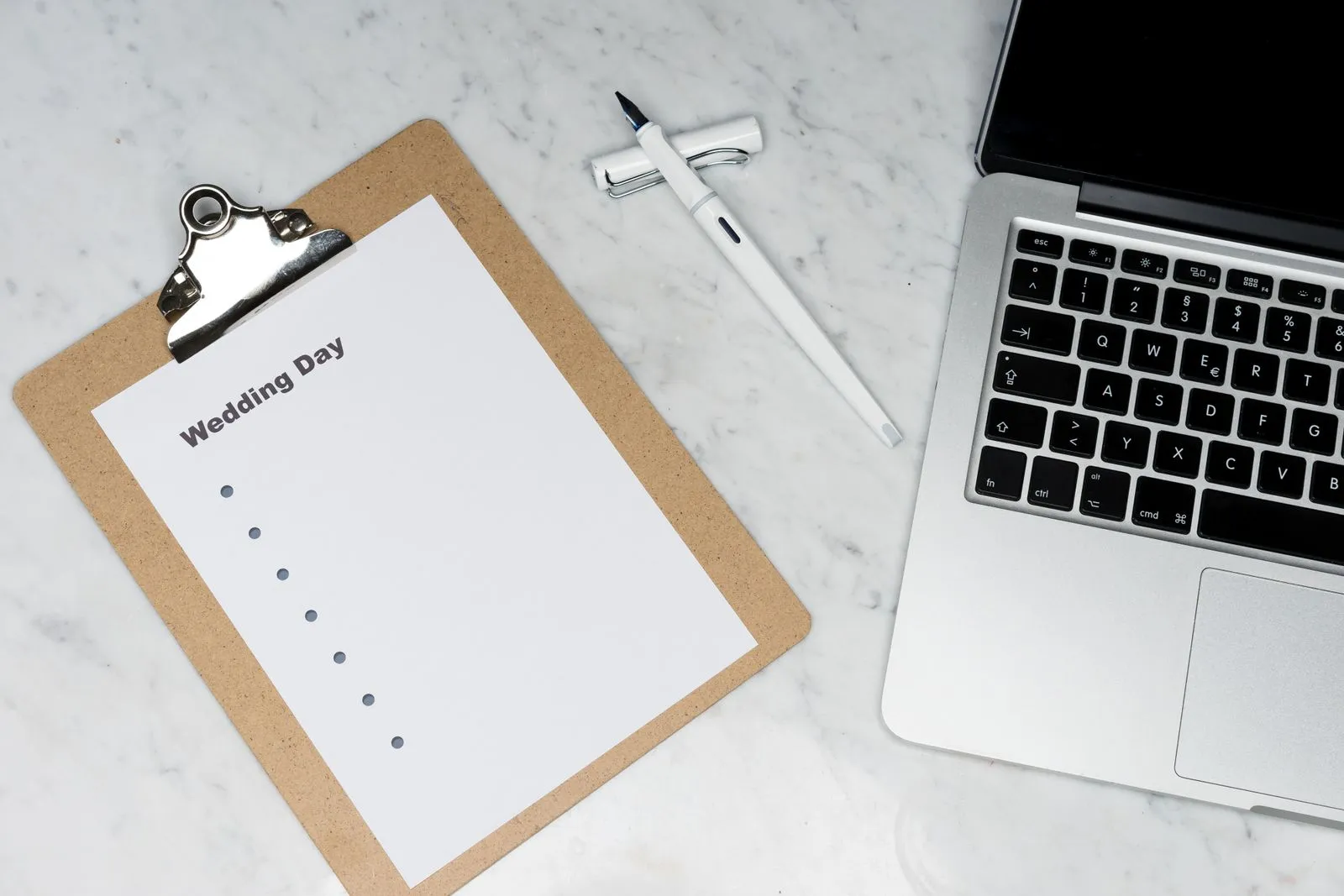 Wedding planning sheet on a clipboard beside a laptop.