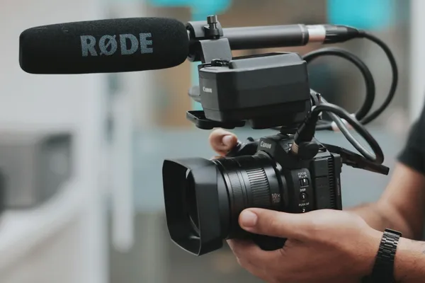 Handheld video camera with a microphone mounted above the lens.