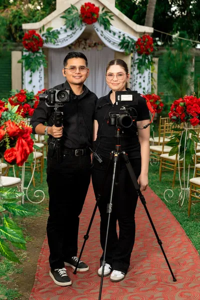 Two people with photography equipment in front of a floral ceremony setting.