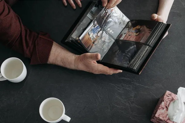 Hands turning the pages of a photo album on a table with two cups.