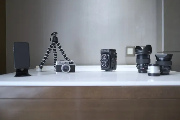 Cameras, lenses and a small tripod arranged on a white table.