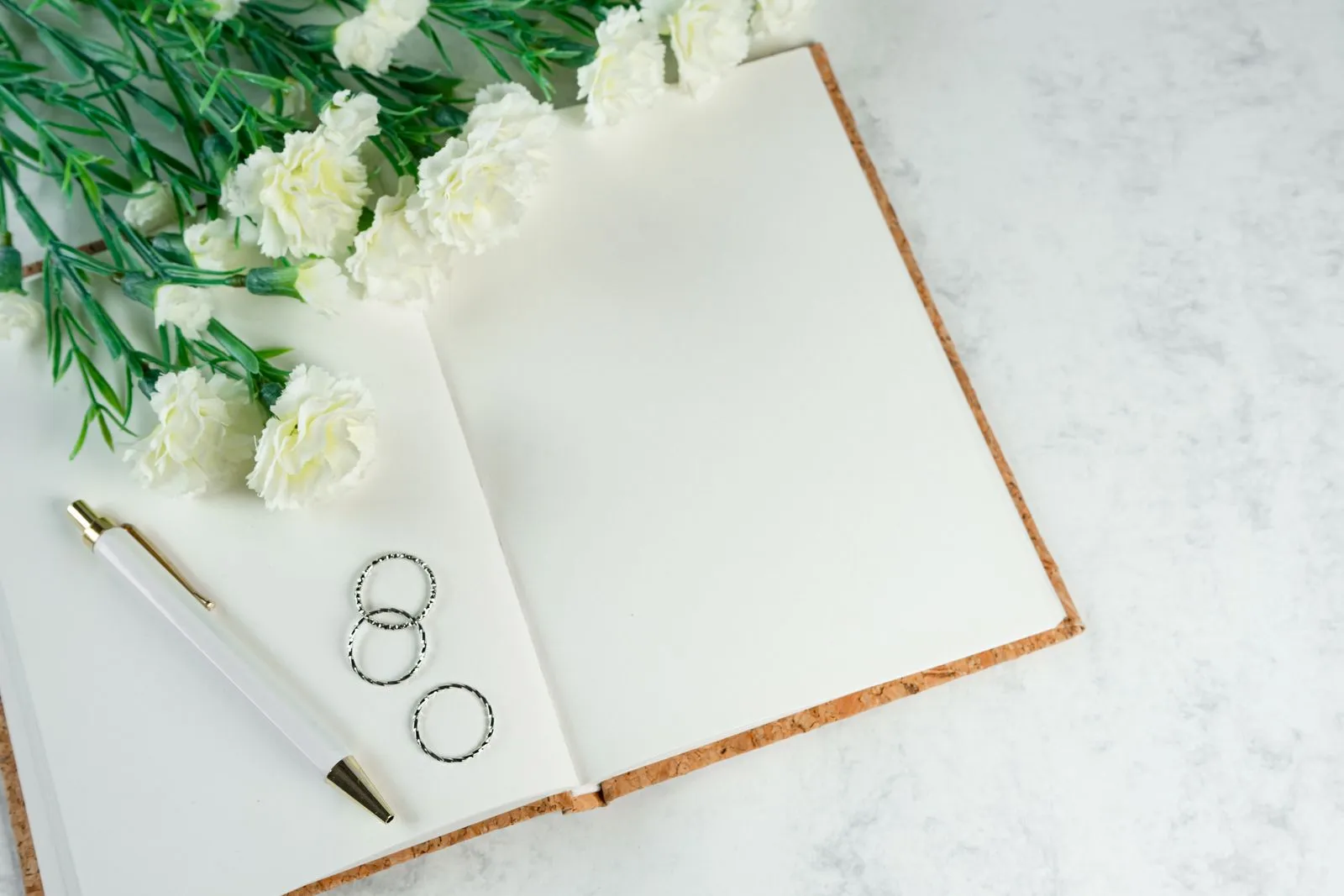 Alliances, stylo et fleurs blanches autour d’un carnet ouvert.