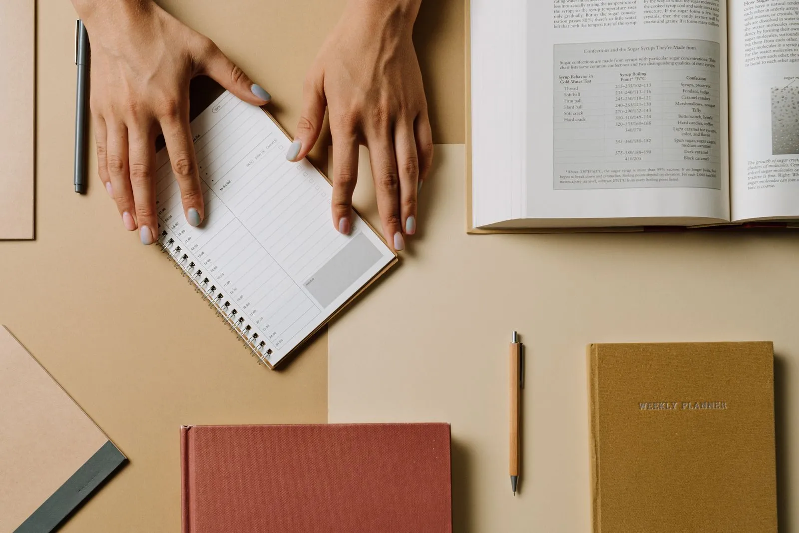 Hands above a planner on a desk with several notebooks.