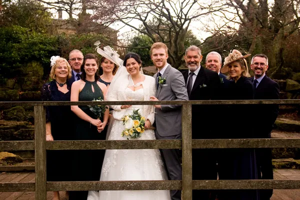 Wedding couple posing with a group of guests behind a wooden fence.