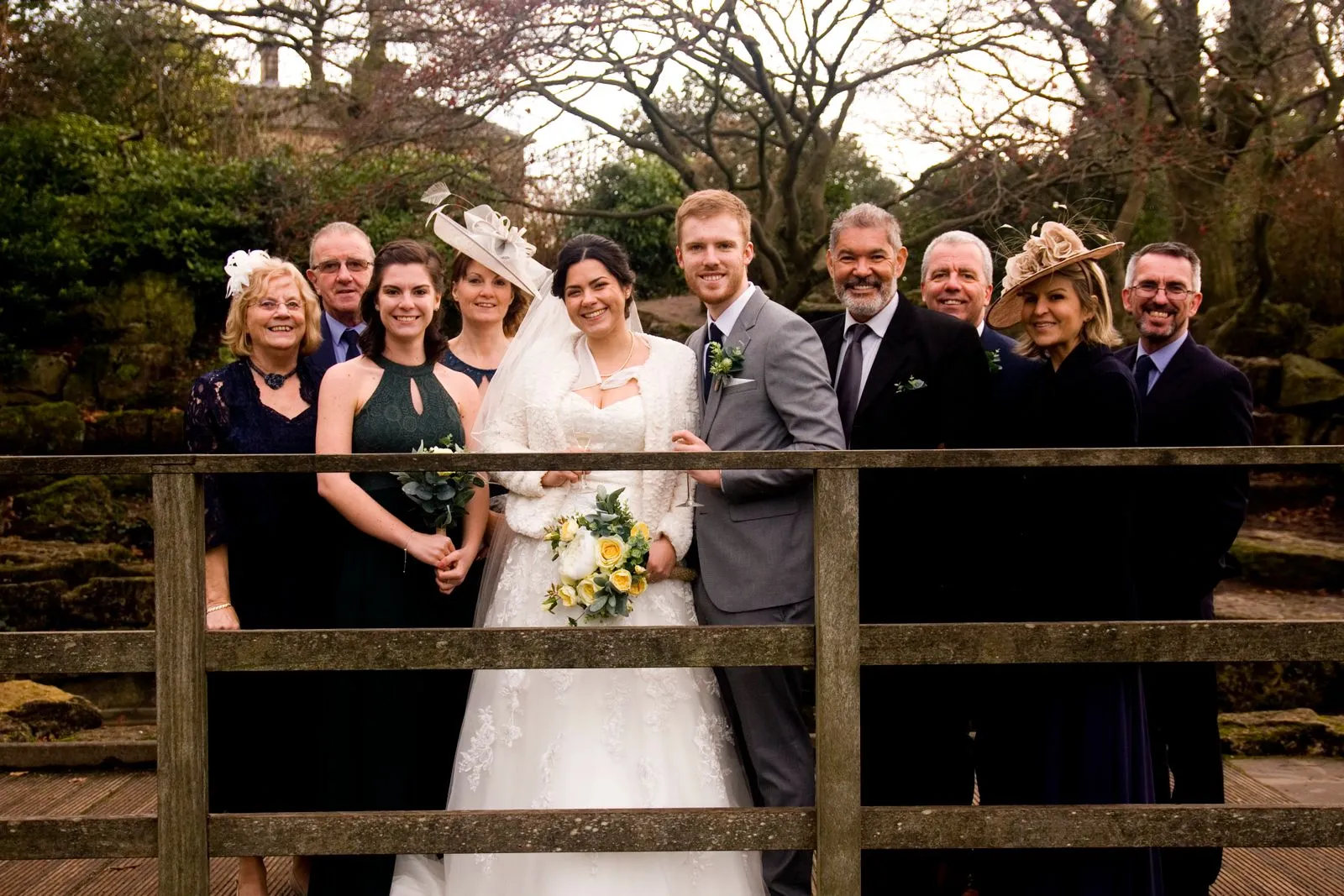 Wedding couple posing with a group of guests behind a wooden fence.