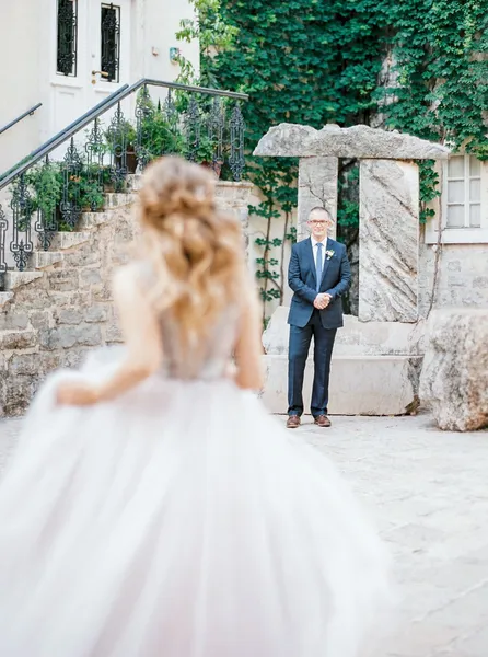 Bride seen from behind walking toward a man in a suit near a staircase.