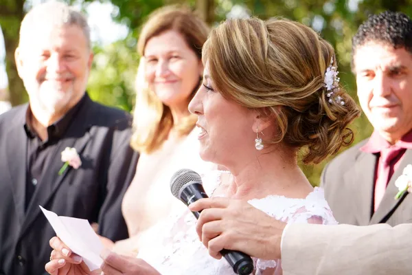 Person holding a microphone and a sheet of paper in front of guests at a wedding.