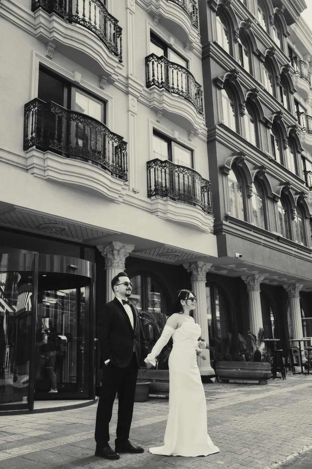Couple in wedding attire in front of a building facade, in black and white.