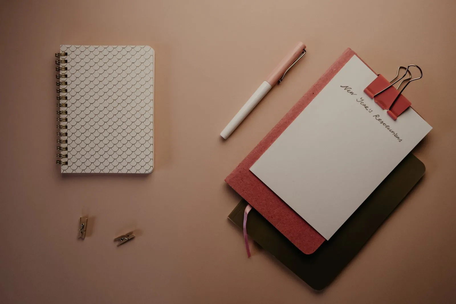 Notebooks and a pen on a desk, with a clip holding sheets of paper.