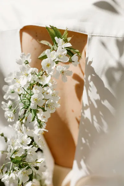 Detail of a wedding dress beside a branch covered in white blossoms.