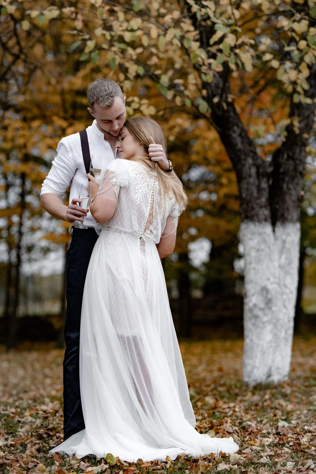Couple en tenue de mariage enlacé dans un parc aux feuilles d’automne.