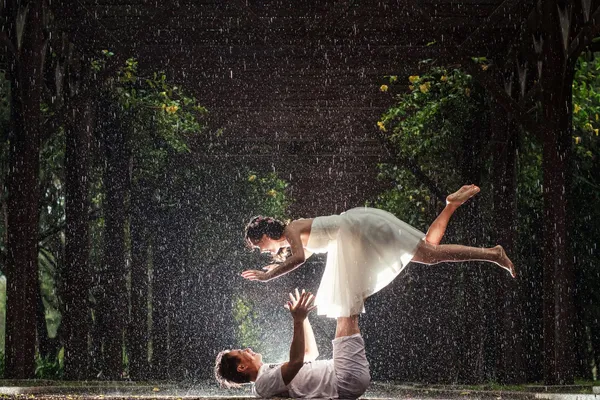 Couple in wedding attire holding a dipped pose in the rain.