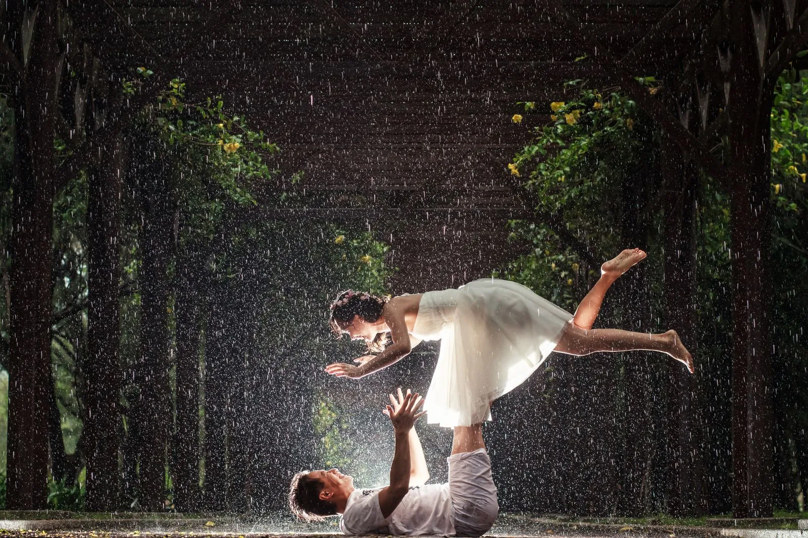 Couple in wedding attire holding a dipped pose in the rain.