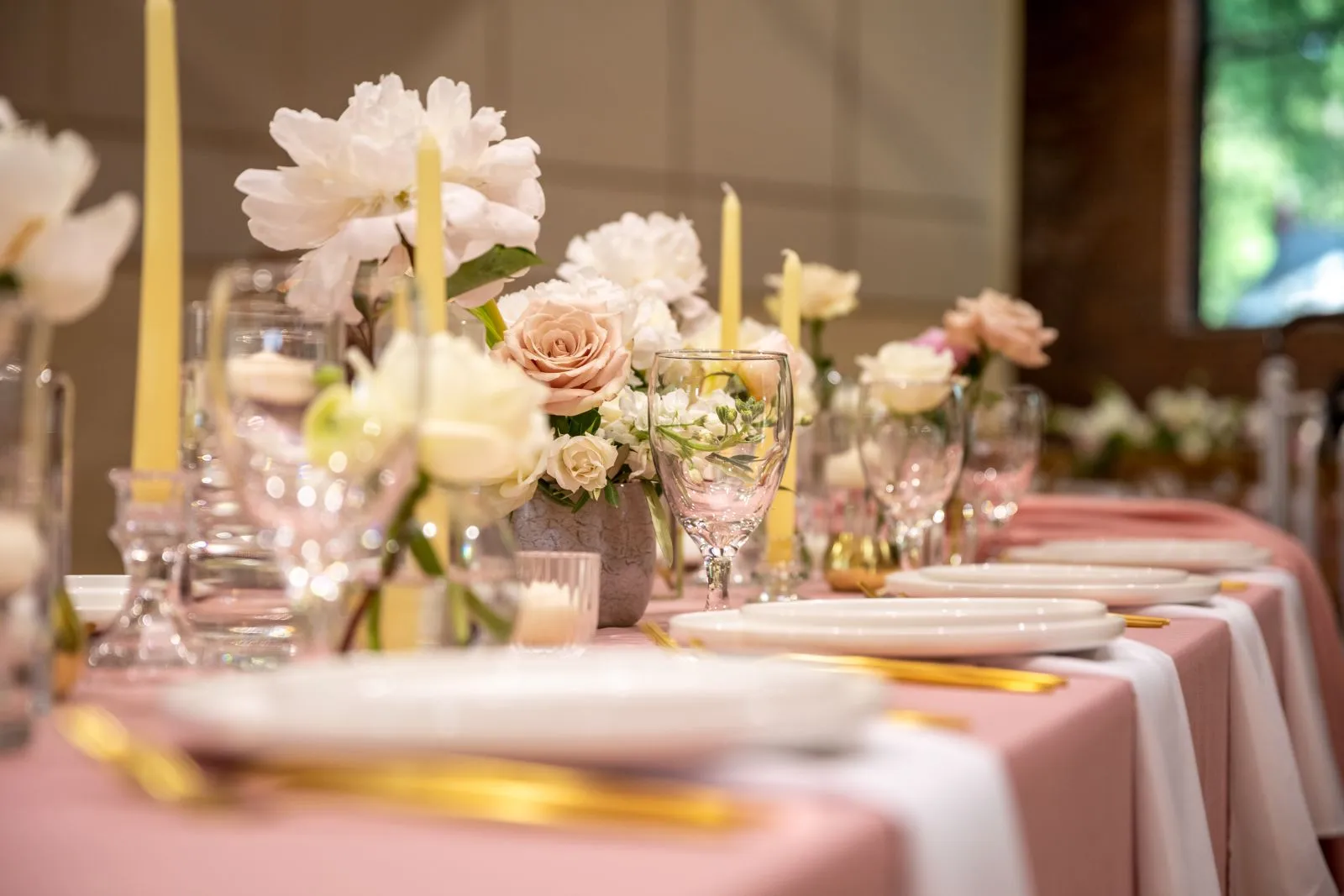 Table de réception décorée de fleurs roses, de vaisselle et de verrerie.