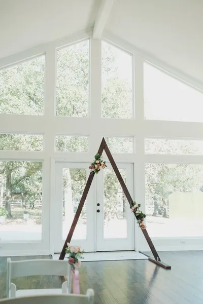Minimalist wedding arch set within a bright, modern interior with large windows and floral decor.