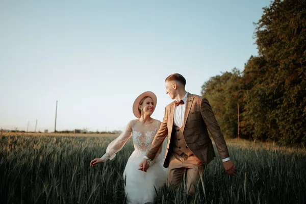 A joyful couple walks hand in hand through a field, capturing a beautiful summer wedding moment.
