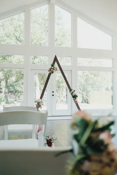 Bright indoor wedding ceremony setup featuring a floral arch and white chairs with natural light.