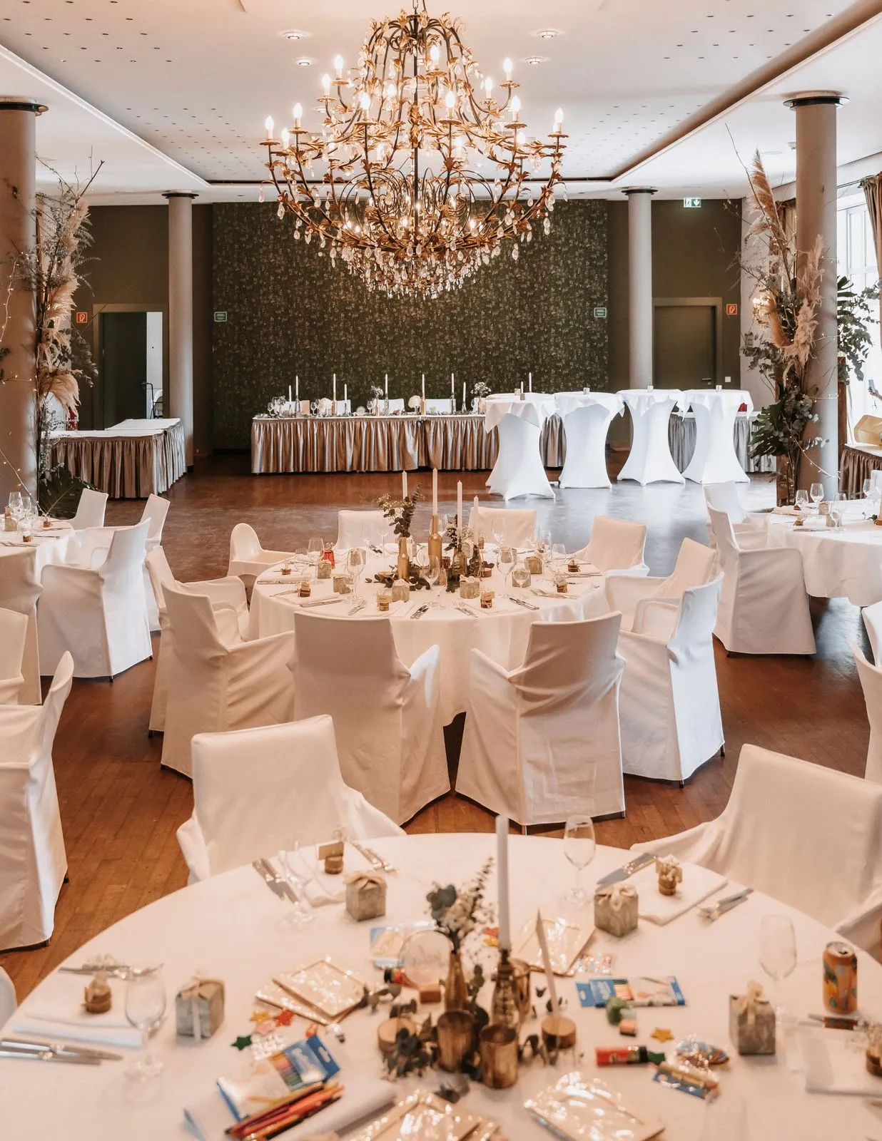 Tables de mariage dressées sous un lustre dans une salle décorée.