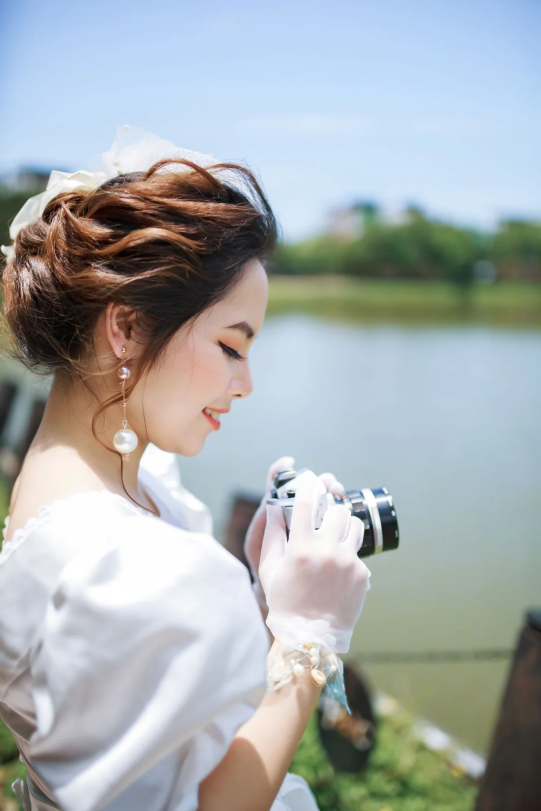 Mariée regardant un appareil photo qu’elle tient dans ses mains au bord d’un lac.