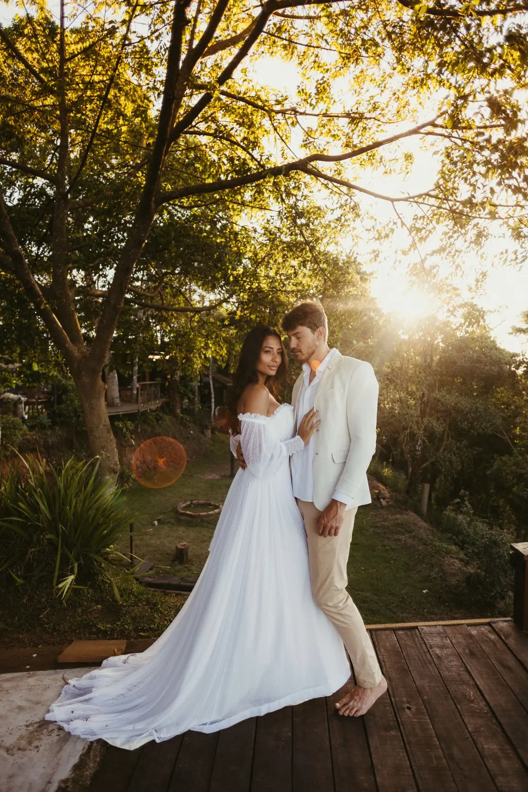 Couple en tenue de mariage enlacé sur une terrasse de bois dans la lumière du soir.
