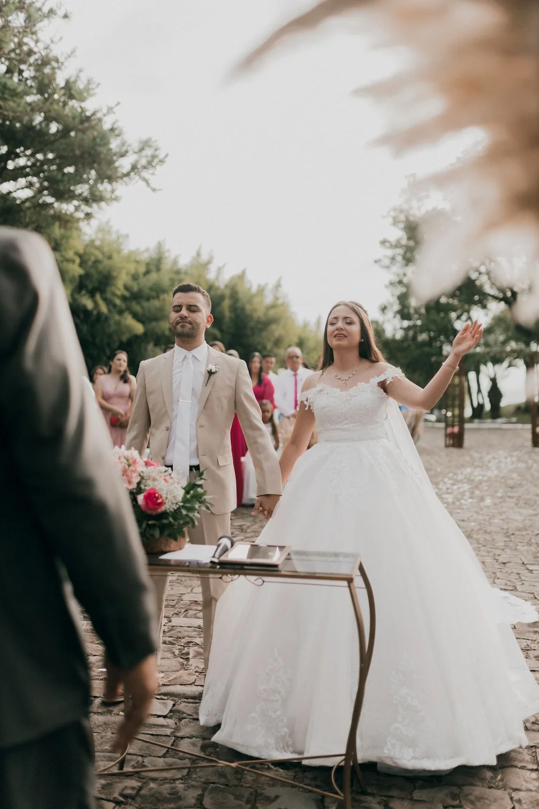 Mariés debout devant une table pendant une cérémonie extérieure entourée d’invités.
