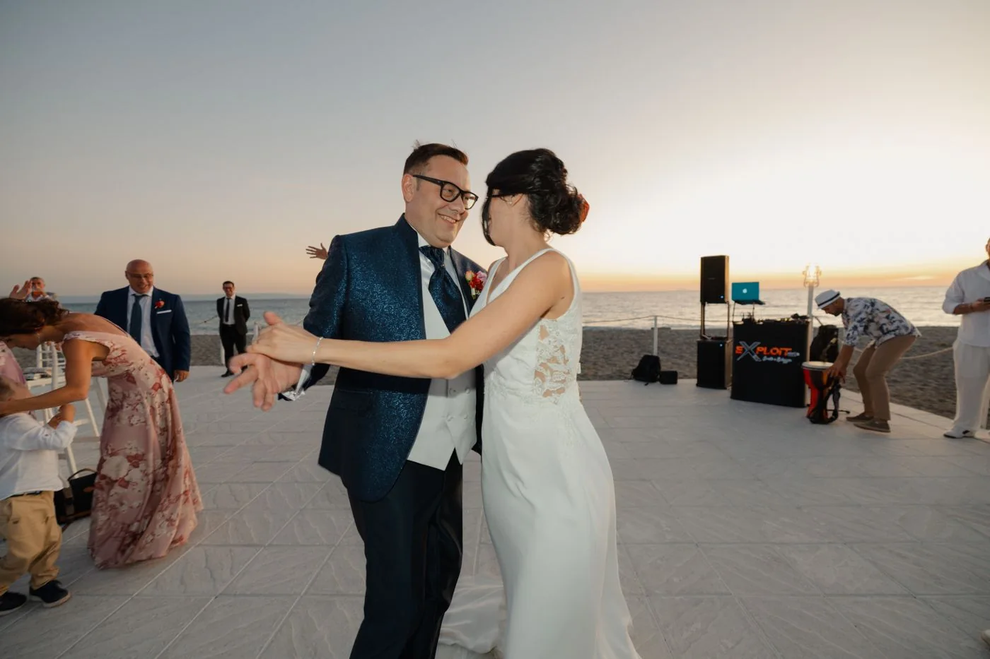 Bride and groom dancing on a seaside terrace at dusk.