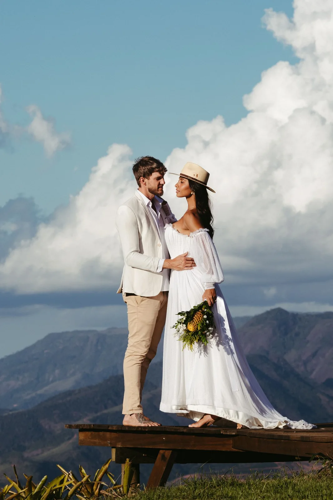 Un couple en tenue de mariage se regarde sur une plateforme de bois devant les montagnes.