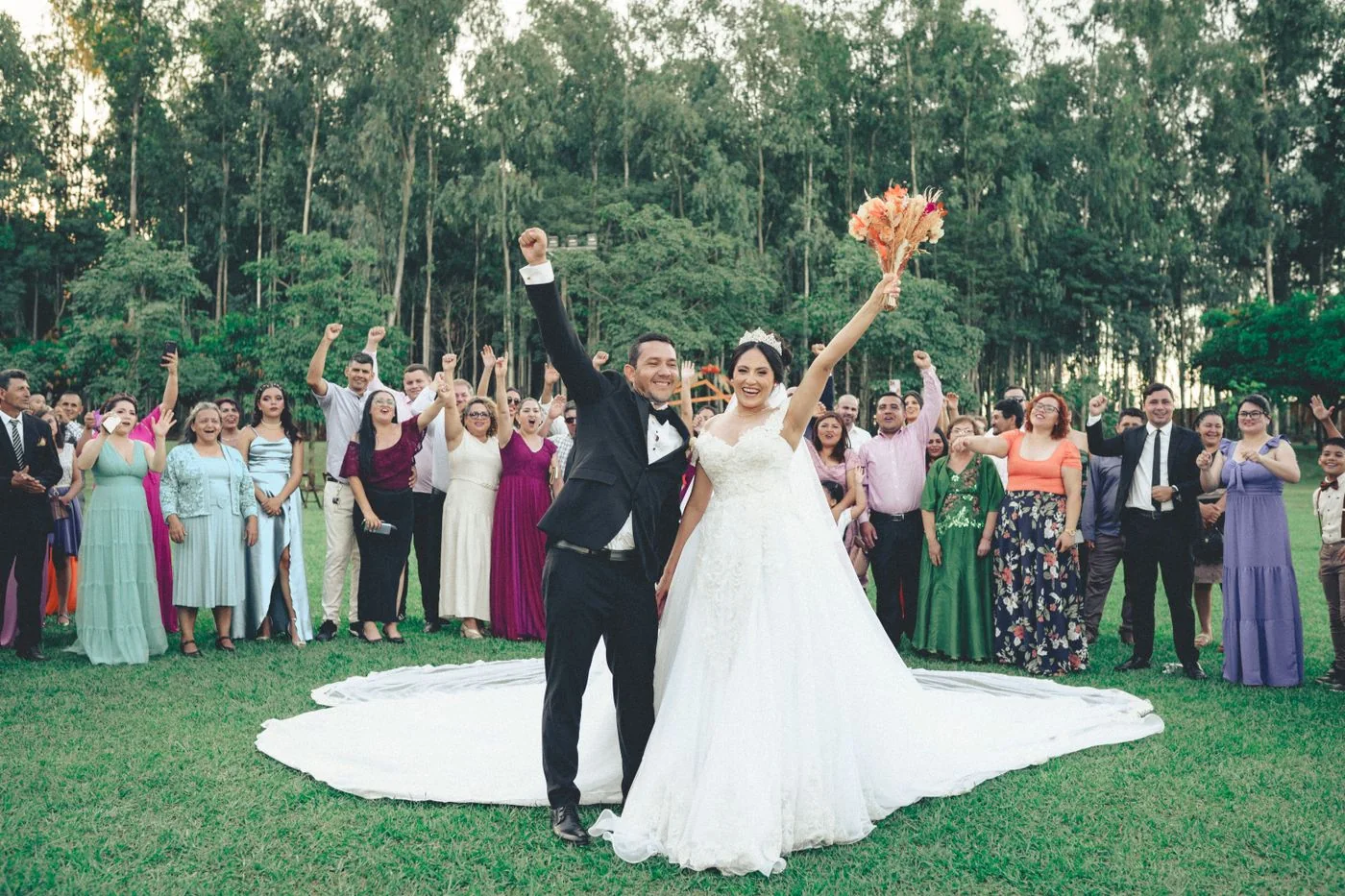 Newlyweds raise their arms in front of guests gathered on a lawn.