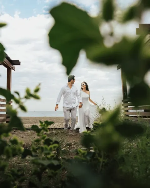 A couple dressed in white descends steps framed by foliage.