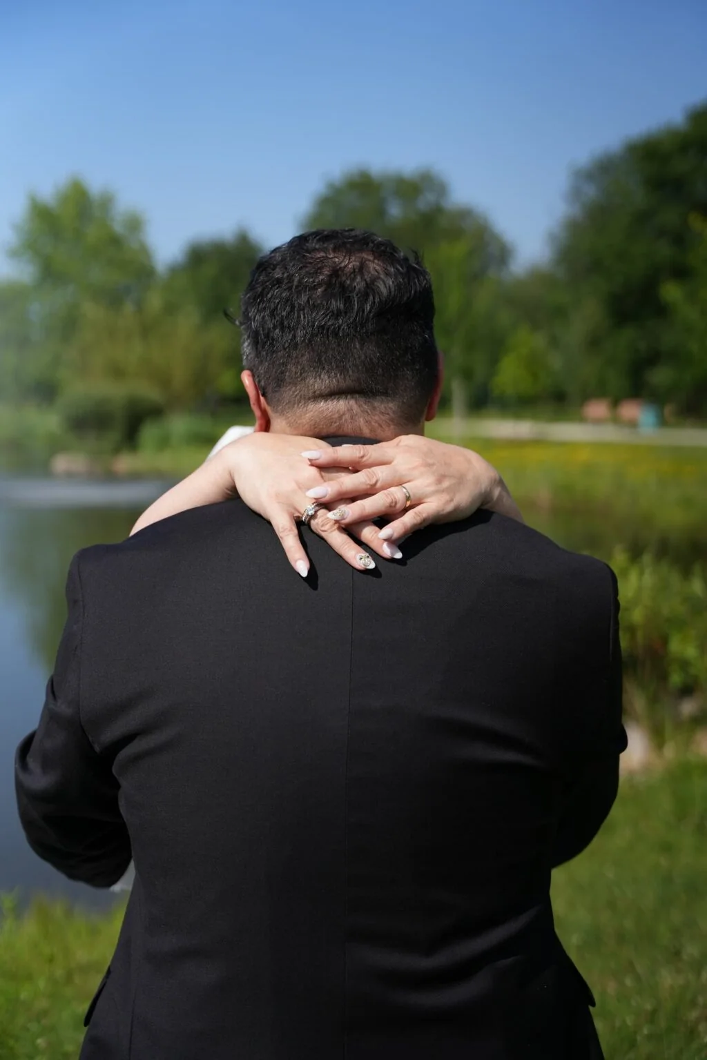 A couple embraces, photographed from behind the groom’s shoulder.
