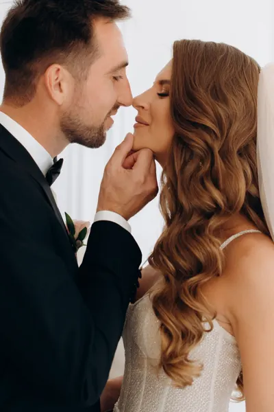 A couple smiles at close range as the groom touches his partner’s chin.