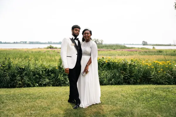A couple in wedding attire poses in a flower-filled meadow.