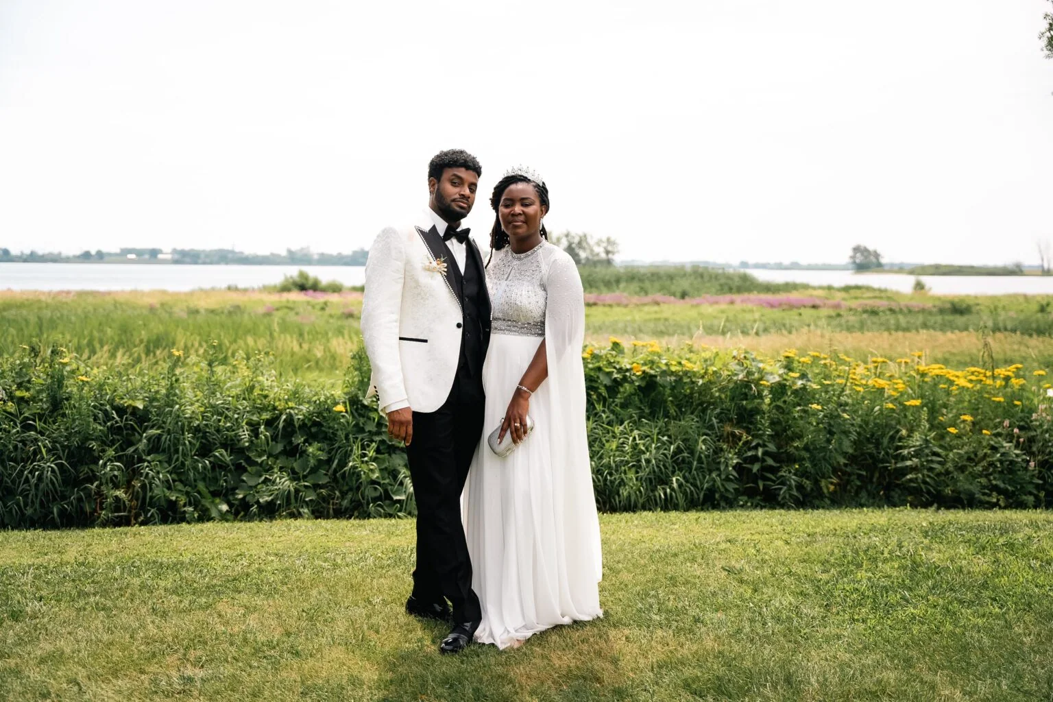 A couple in wedding attire poses in a flower-filled meadow.