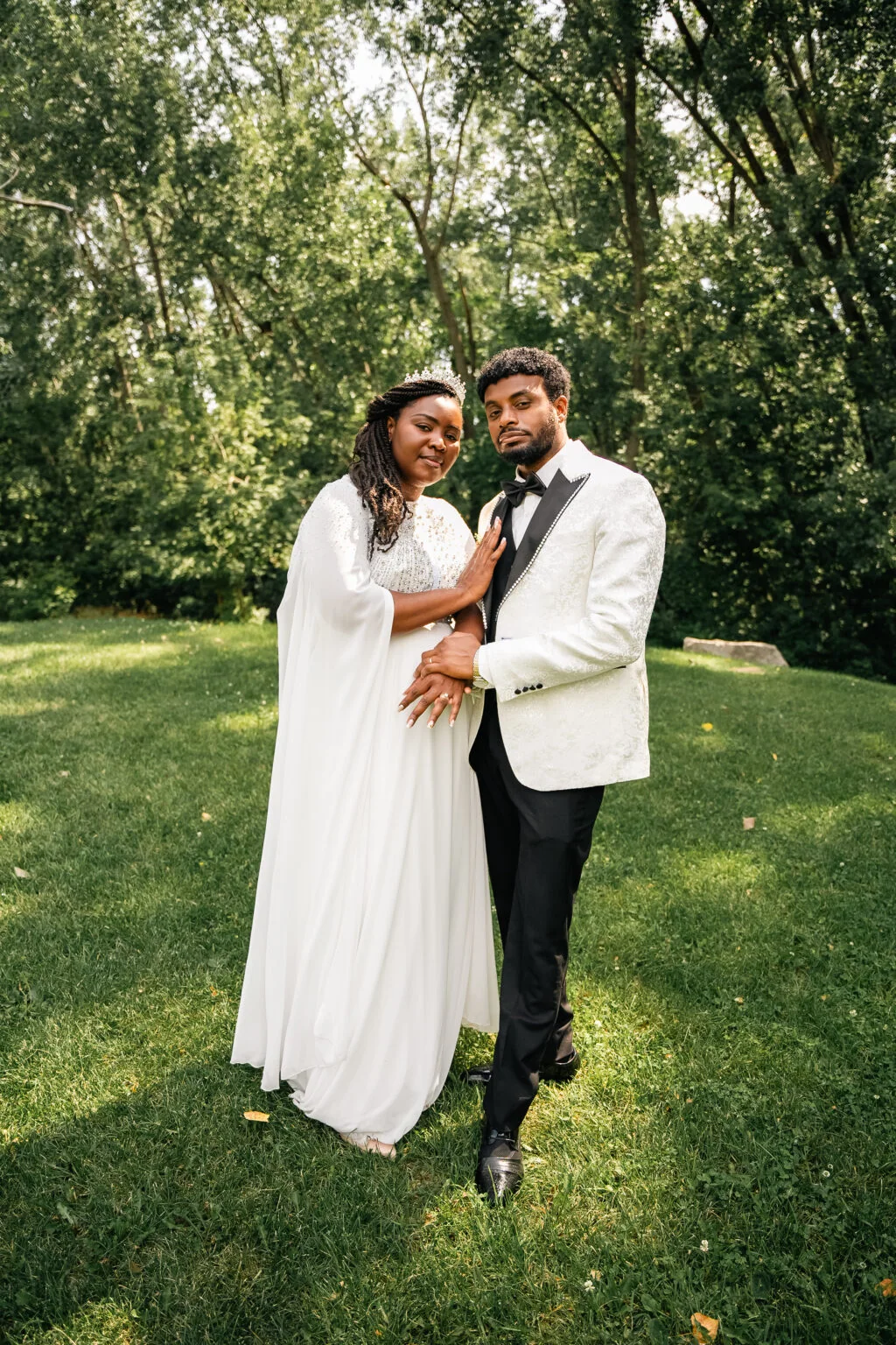 A couple in wedding attire embraces in a shaded garden.