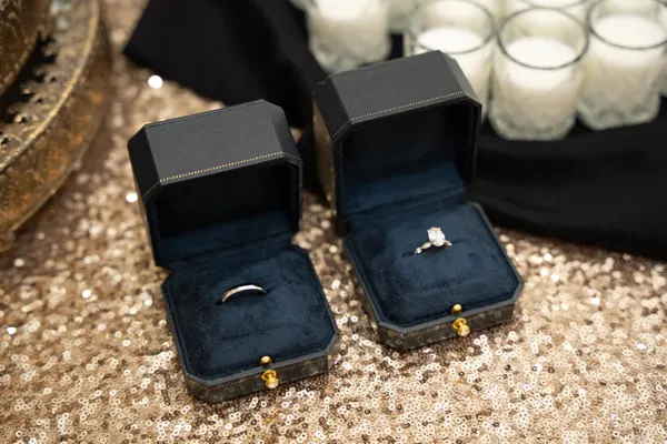 Two wedding rings rest in open boxes beside candles.