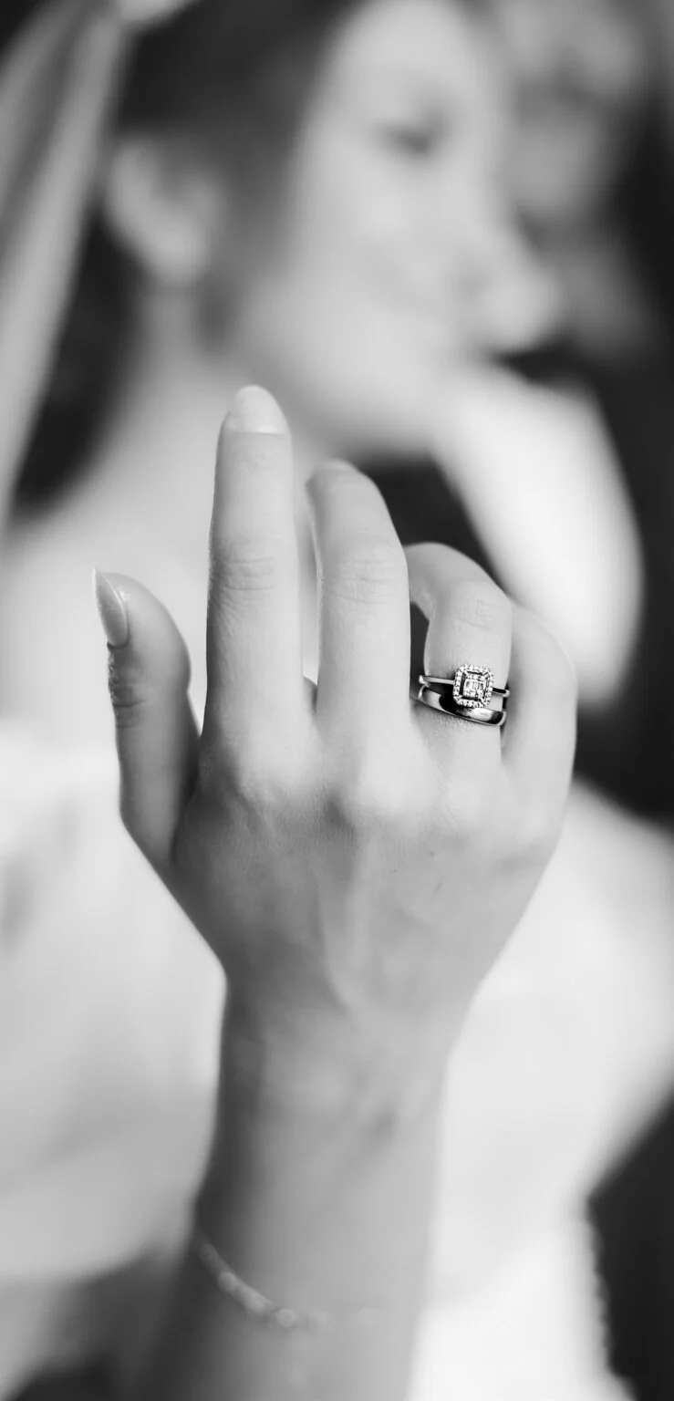 Black-and-white close-up of an engagement ring worn on a hand.