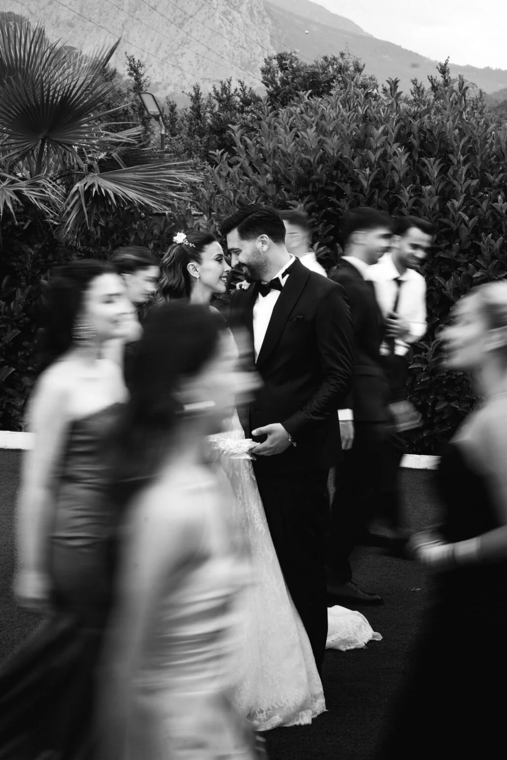 A group in formal attire crosses a garden in a black-and-white photograph.