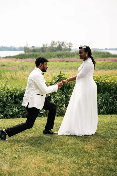 A man kneels before his partner in a sunlit meadow.