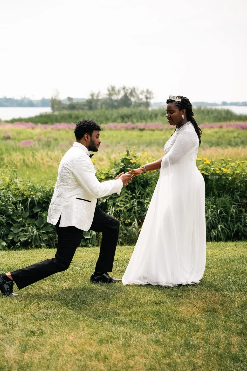 A man kneels before his partner in a sunlit meadow.