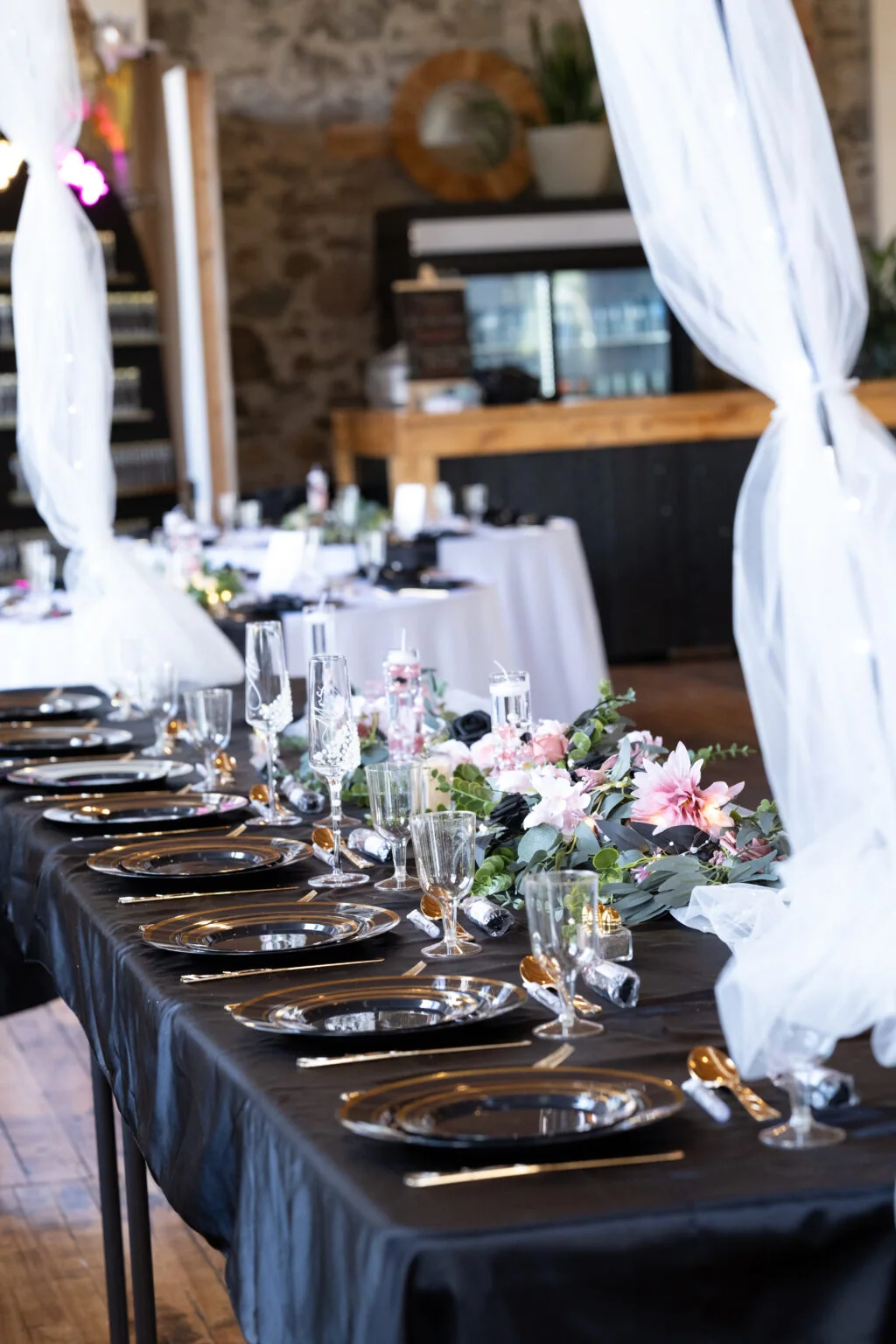 A long reception table is set with flowers and glassware.