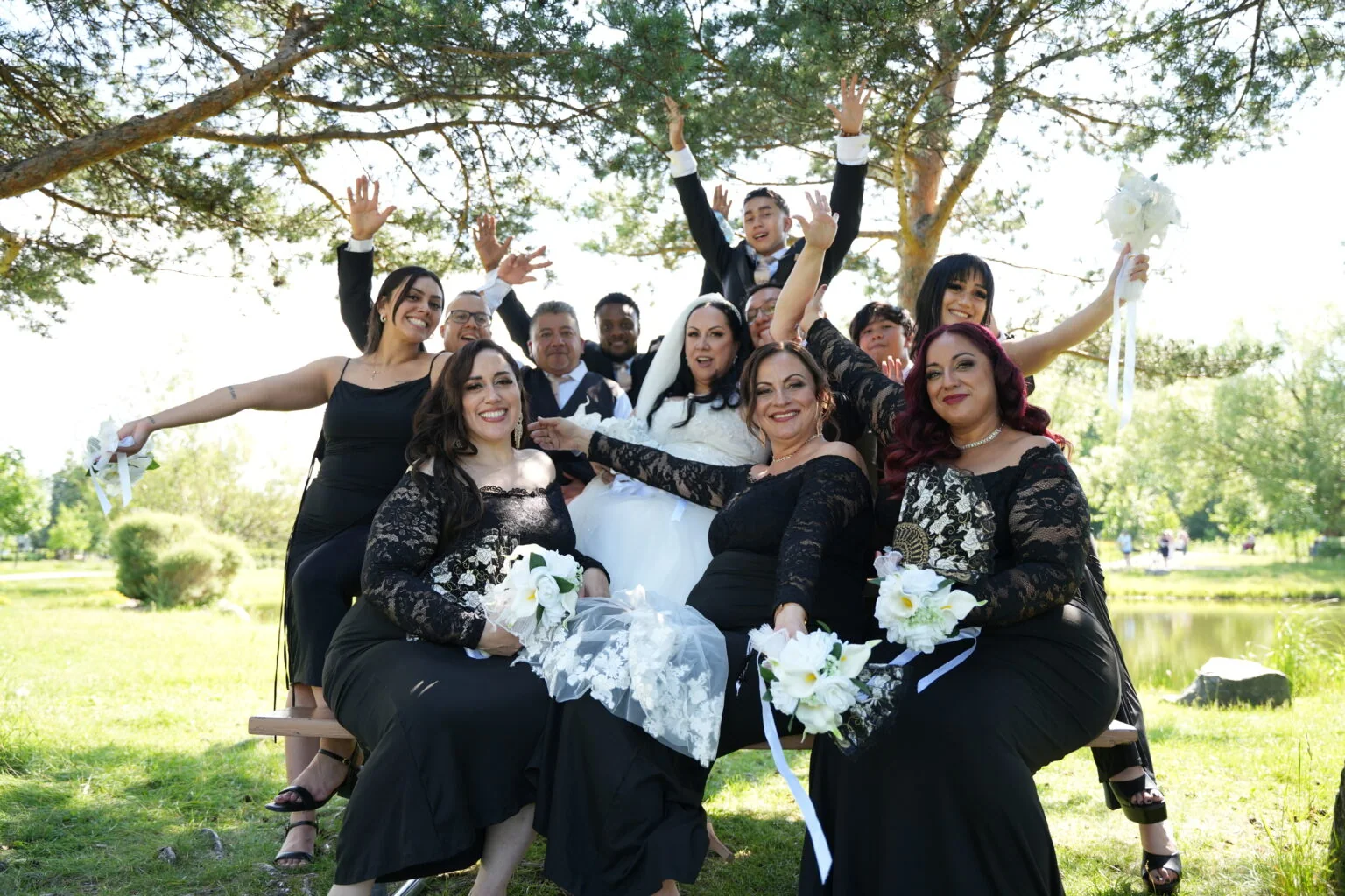 La mariée et ses proches posent ensemble, les bras levés sous un arbre.