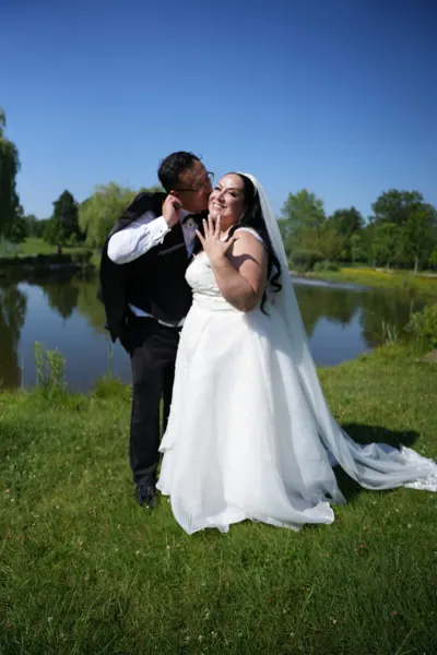 The newlyweds kiss on a lawn beside the water.
