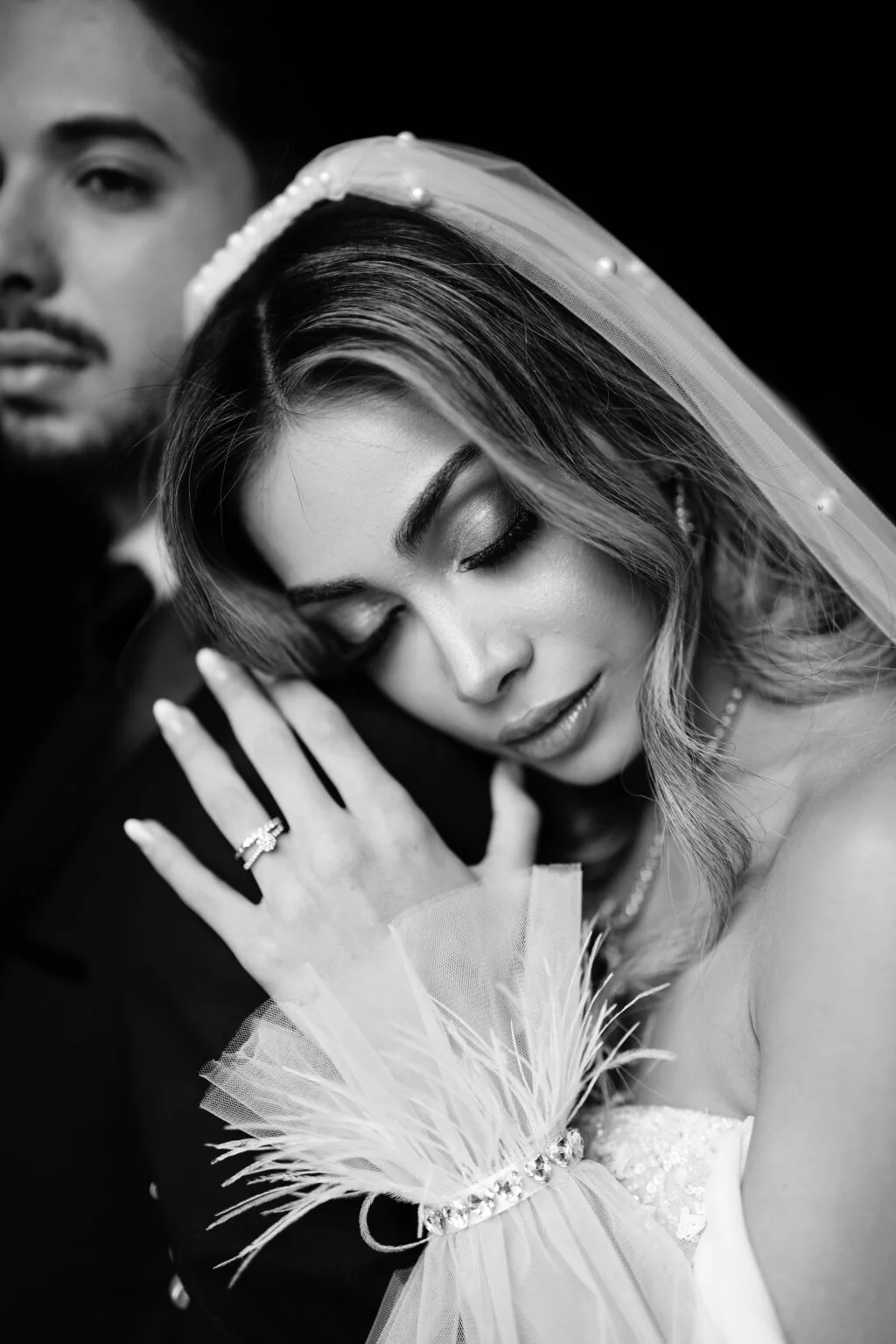 Portrait en noir et blanc d’un couple, la mariée appuyée contre son partenaire.